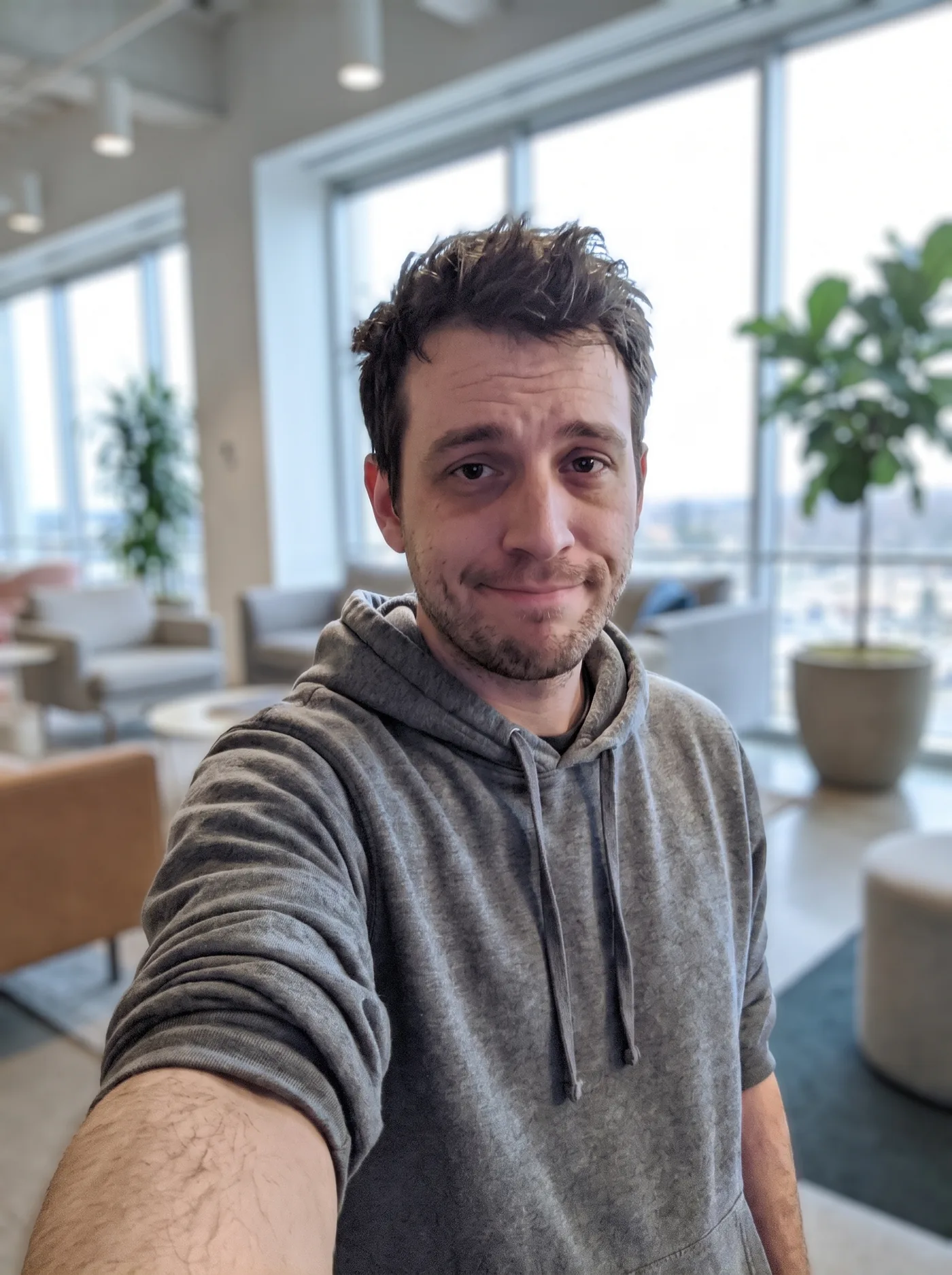 The same selfie with the living room replaced by a bright modern office lounge background.