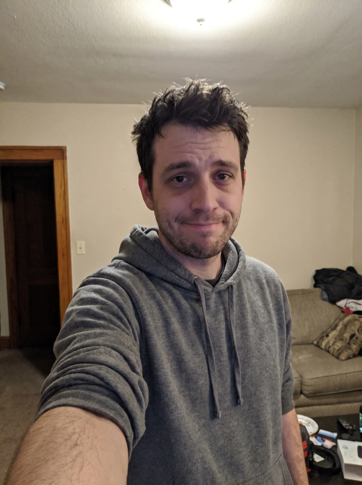 An ordinary AI-generated phone selfie of a man in a grey hoodie in a plain living room, used as the input for every edit in this post.