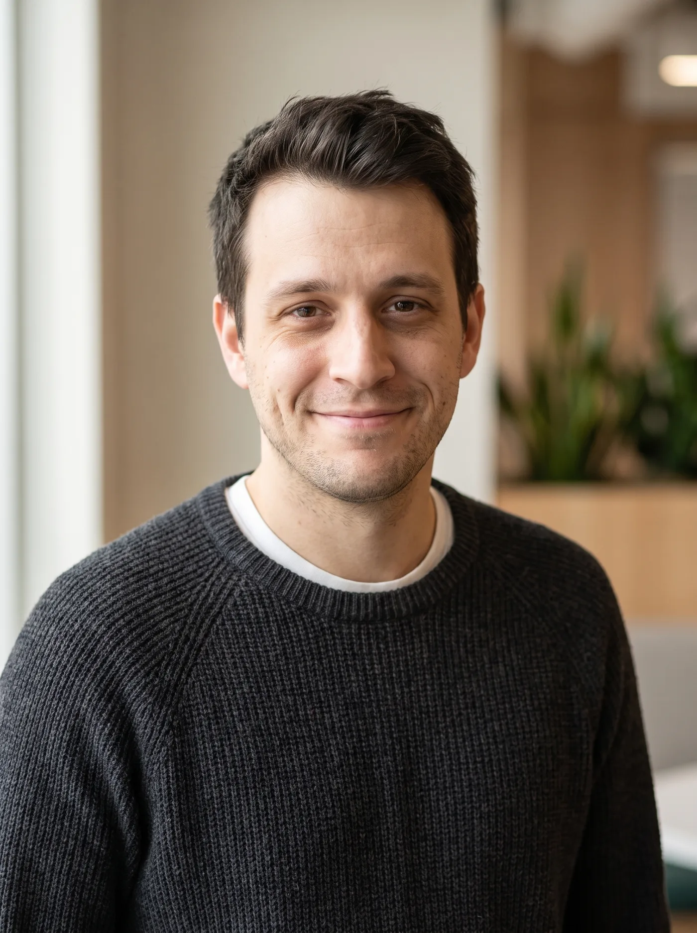 AI-edited LinkedIn-style headshot of the same man in a charcoal crew-neck against a blurred office background.
