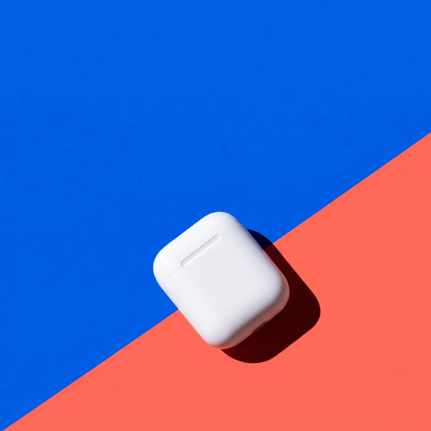 AI-generated colour-blocked ad image of white earbuds on a diagonal cobalt blue and coral background with empty headline space.