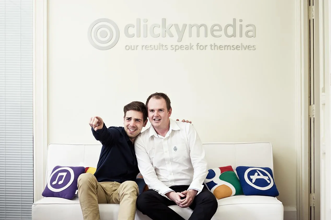 Two of the team on the sofa under the Clicky Media logo