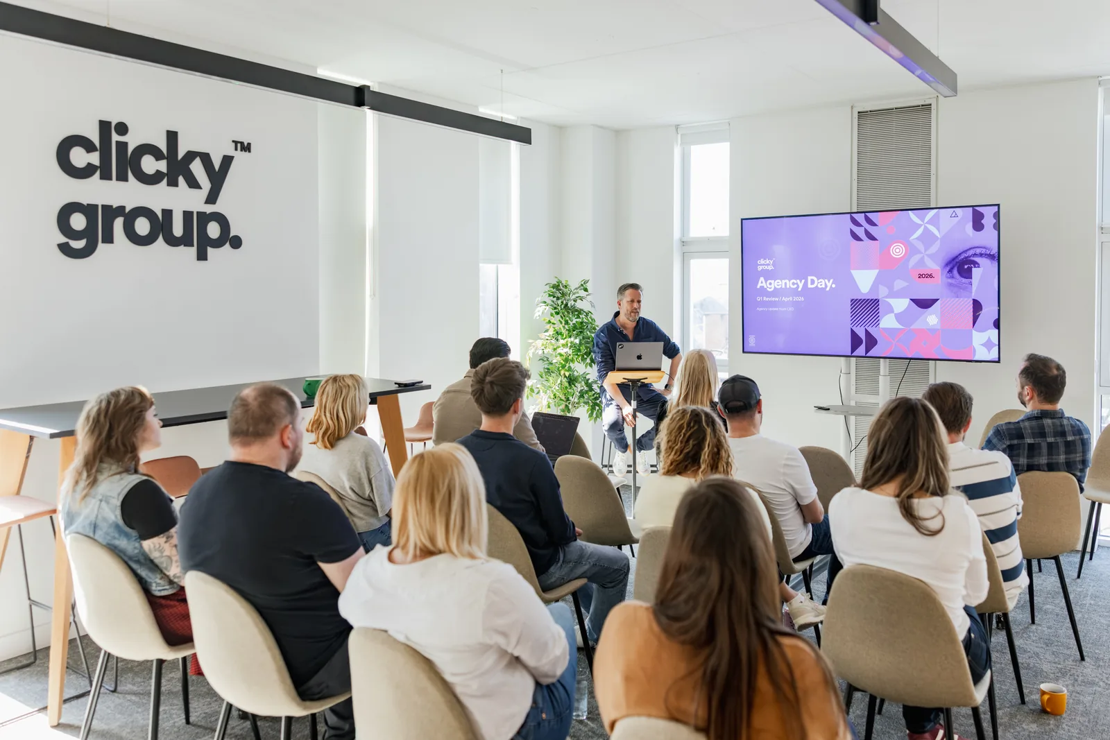 Oli presenting at Agency Day with the Agency Day slide on screen and the full team watching